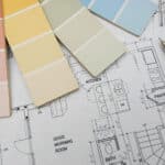 Color swatches in pastel shades are arranged on top of architectural floor plans. A blue pen is placed next to the plans, which include labels for rooms like 'KITCHEN,' 'PANTRY,' and 'BATH.'