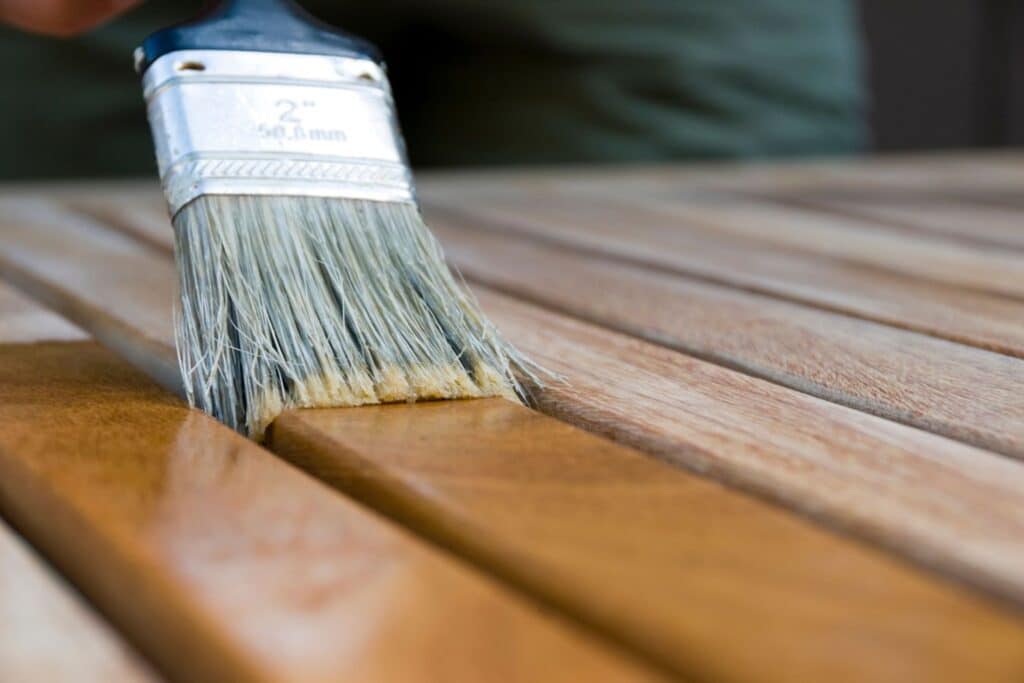 A close-up of a paintbrush applying finish to a wooden surface, highlighting the brush bristles and the smooth wood texture.